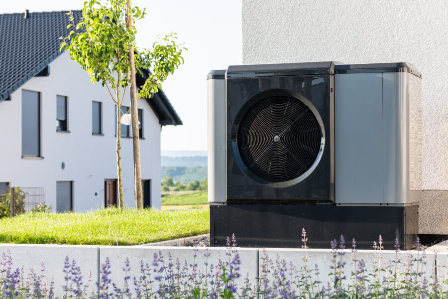 Luftwärmepumpe neben einem modernen Haus, im Vordergrund blühende Pflanzen.
