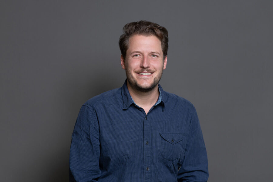 Ein Mann in blauem Hemd vor grauem Hintergrund.