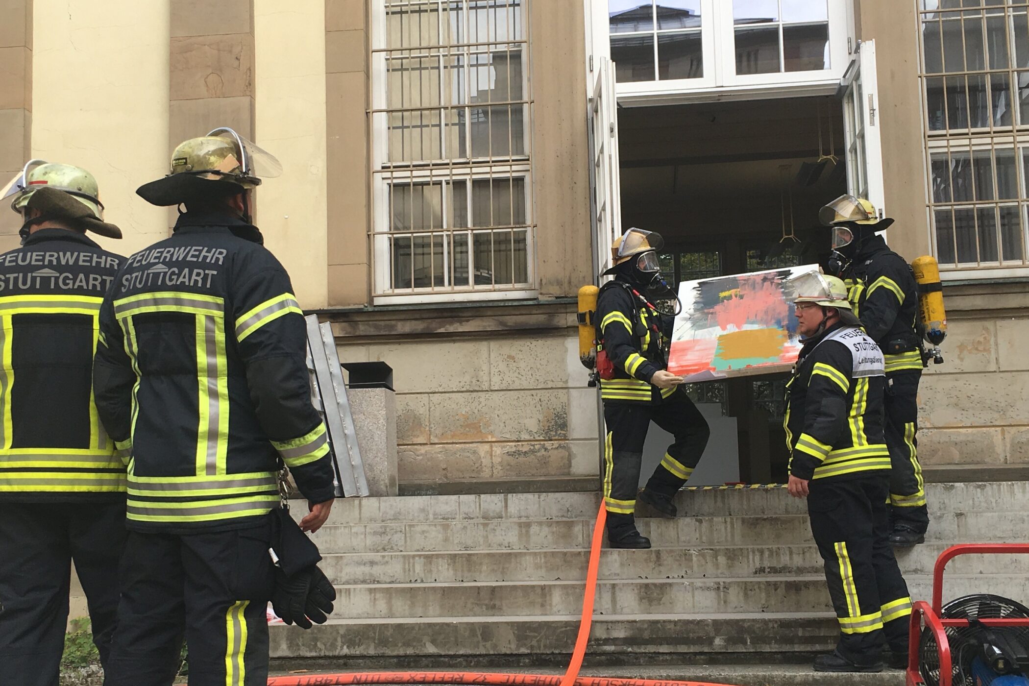 Fünf Feuerwehrleute in Schutzkleidung tragen Gemälde aus einem Gebäude.