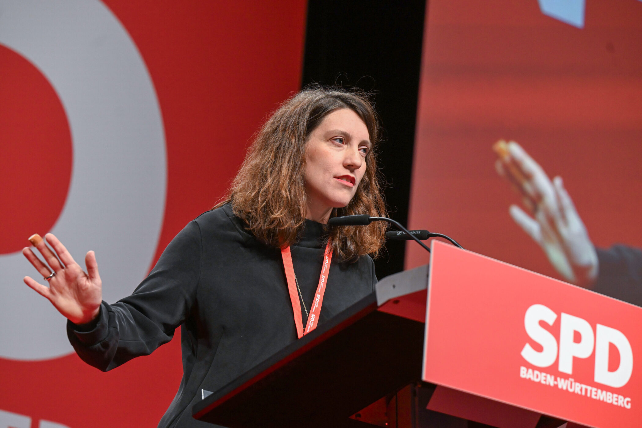 Frau spricht an einem Rednerpult, Hintergrund mit SPD-Logo.