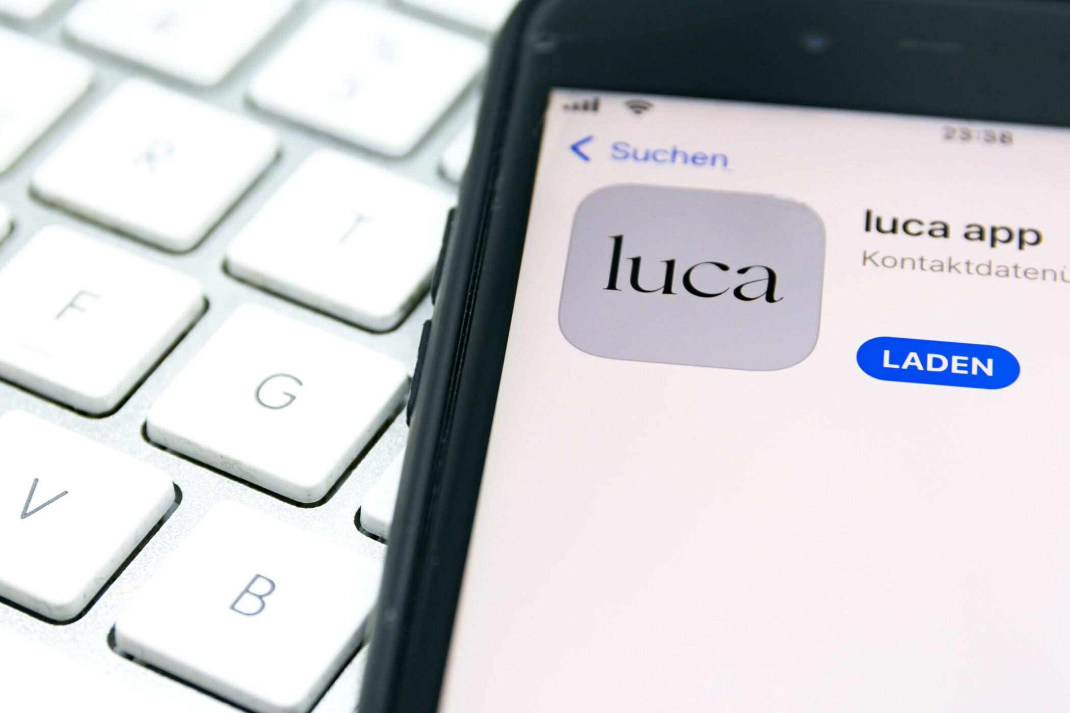 Smartphone zeigt die Luca-App mit "Laden"-Button, daneben weiße Tastatur.