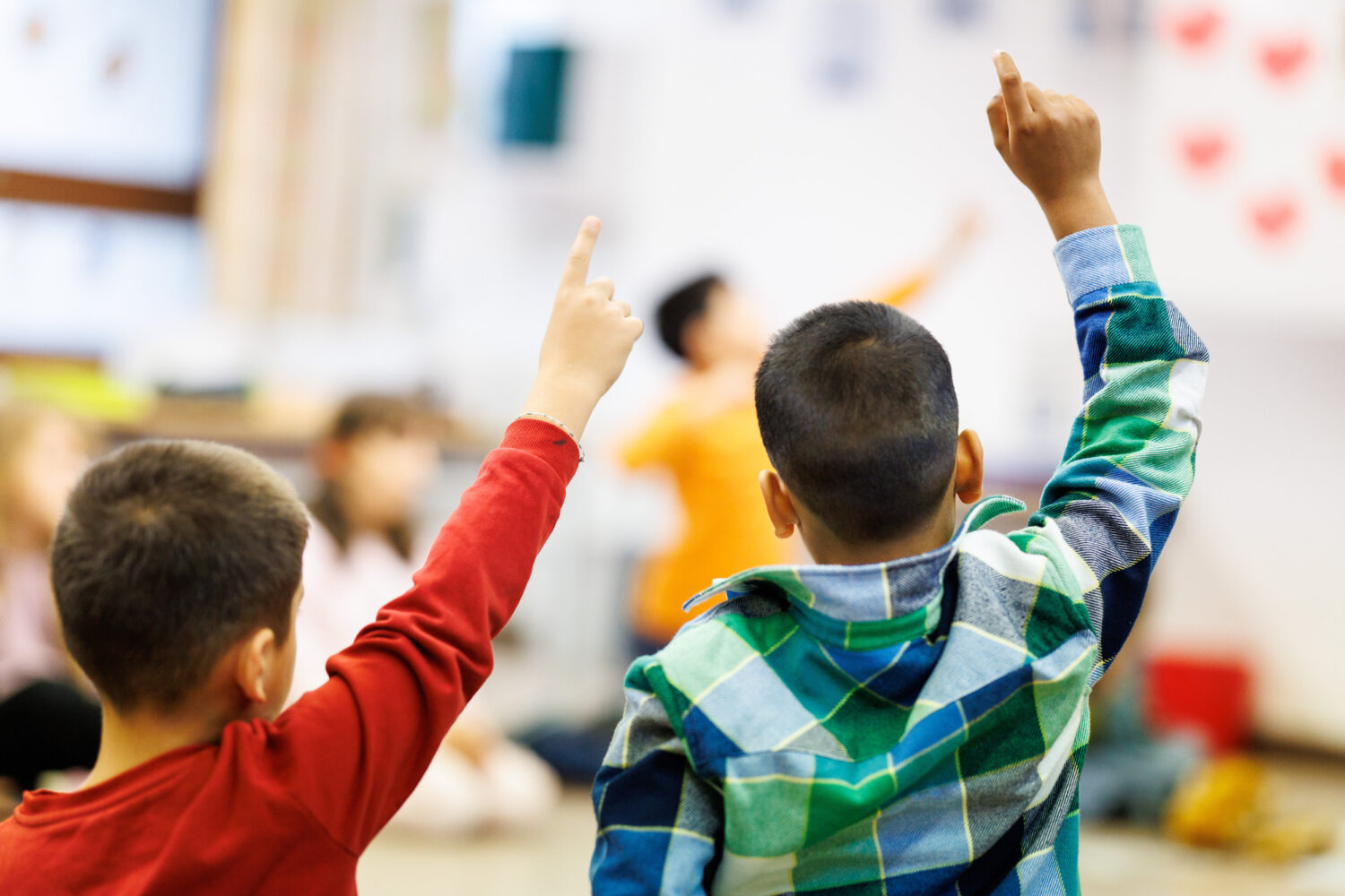 Zwei Kinder mit erhobenen Händen in einem Klassenzimmer.