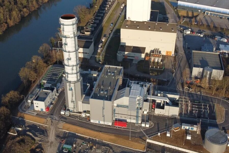 Industrieanlage mit Schornstein, Gebäuden und Straßen, angrenzend an einen Fluss.