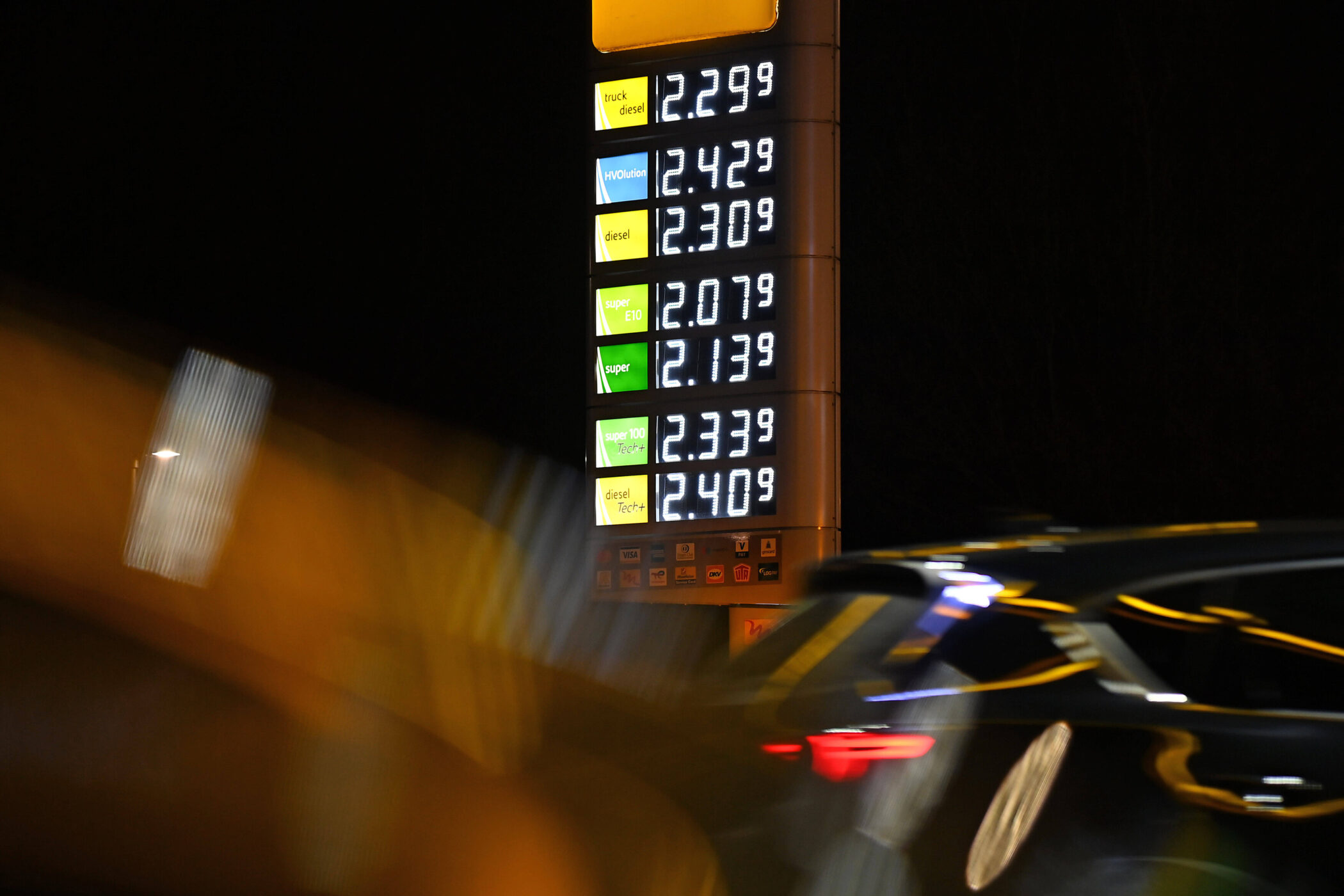 Preistafel an Tankstelle bei Nacht, Auto im Vordergrund. Preise: Diesel 2,30, Super 2,13.