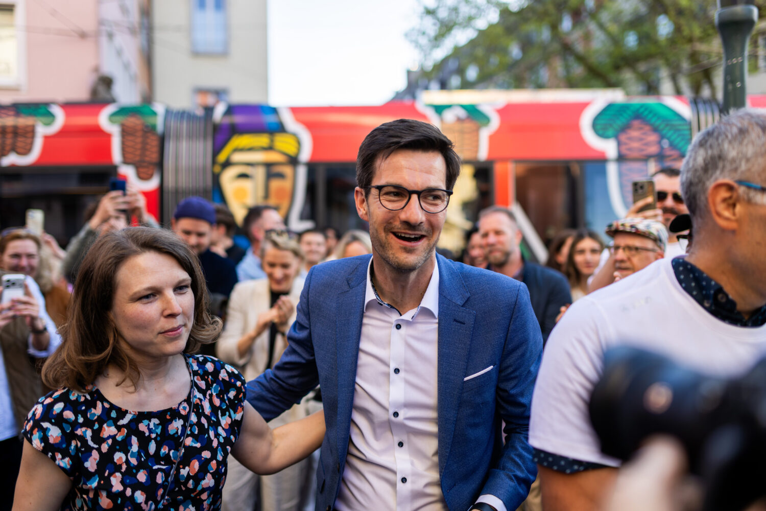 Eine Gruppe von Personen im Freien vor einer rot bemalten Straßenbahn.