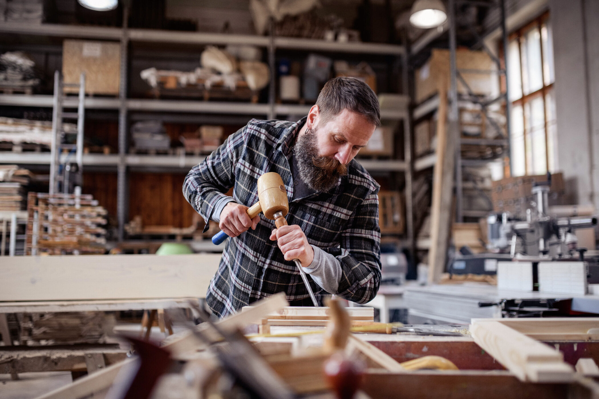 Mann arbeitet mit einem Hammer und Meißel in einer Werkstatt. Regal im Hintergrund.