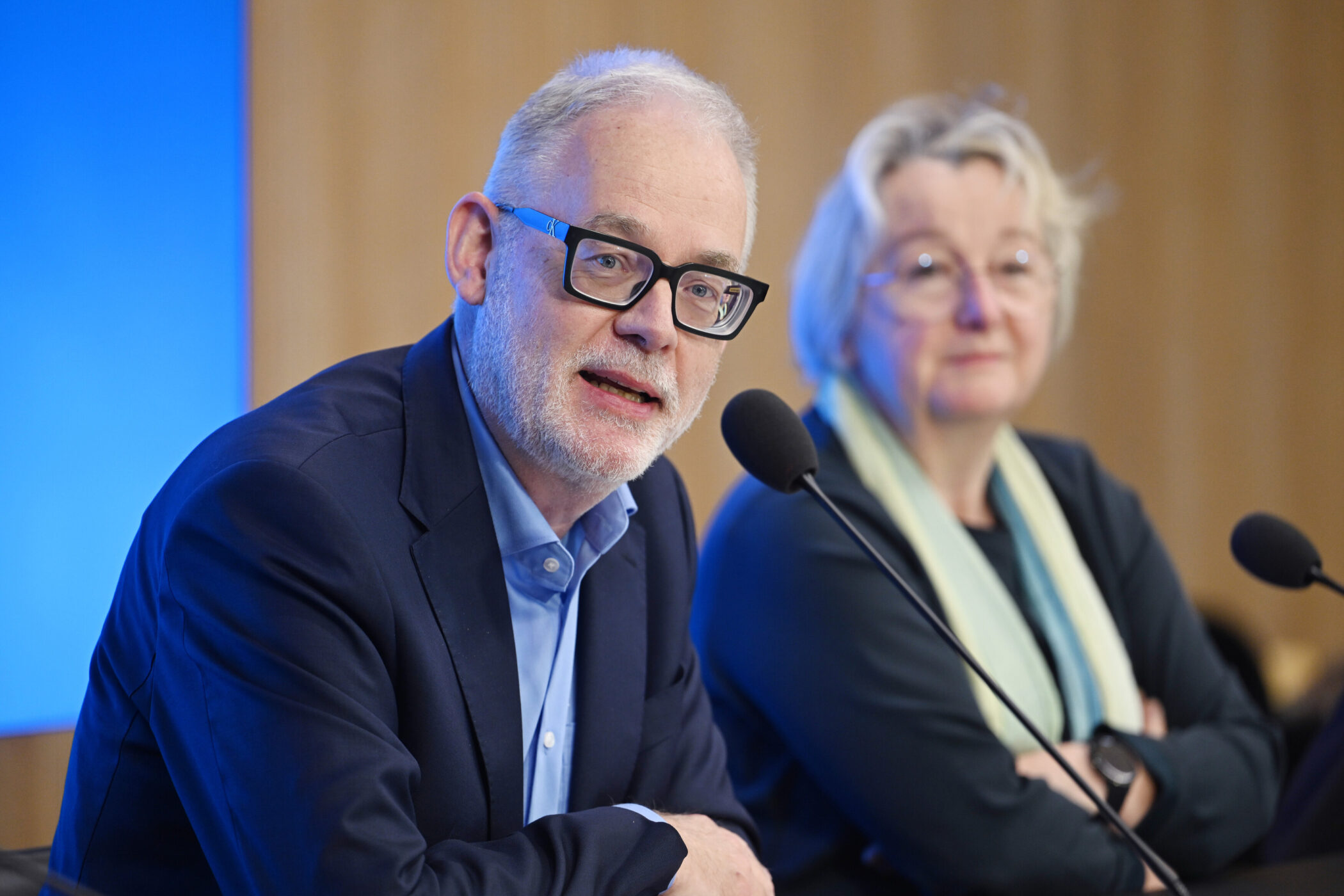 Zwei Personen sprechen in Mikrofone bei einer Veranstaltung.