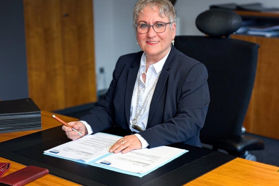 Person in Anzug am Schreibtisch, hält einen Stift, vor Dokumenten.