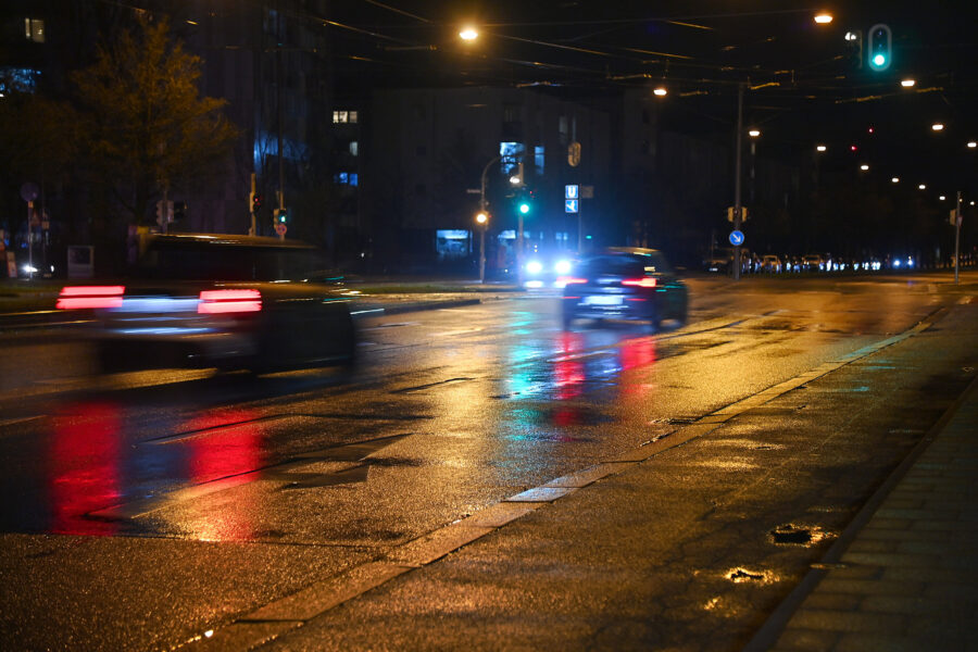 Nasse, beleuchtete Stadtstraße bei Nacht mit fahrenden Autos und Ampel.
