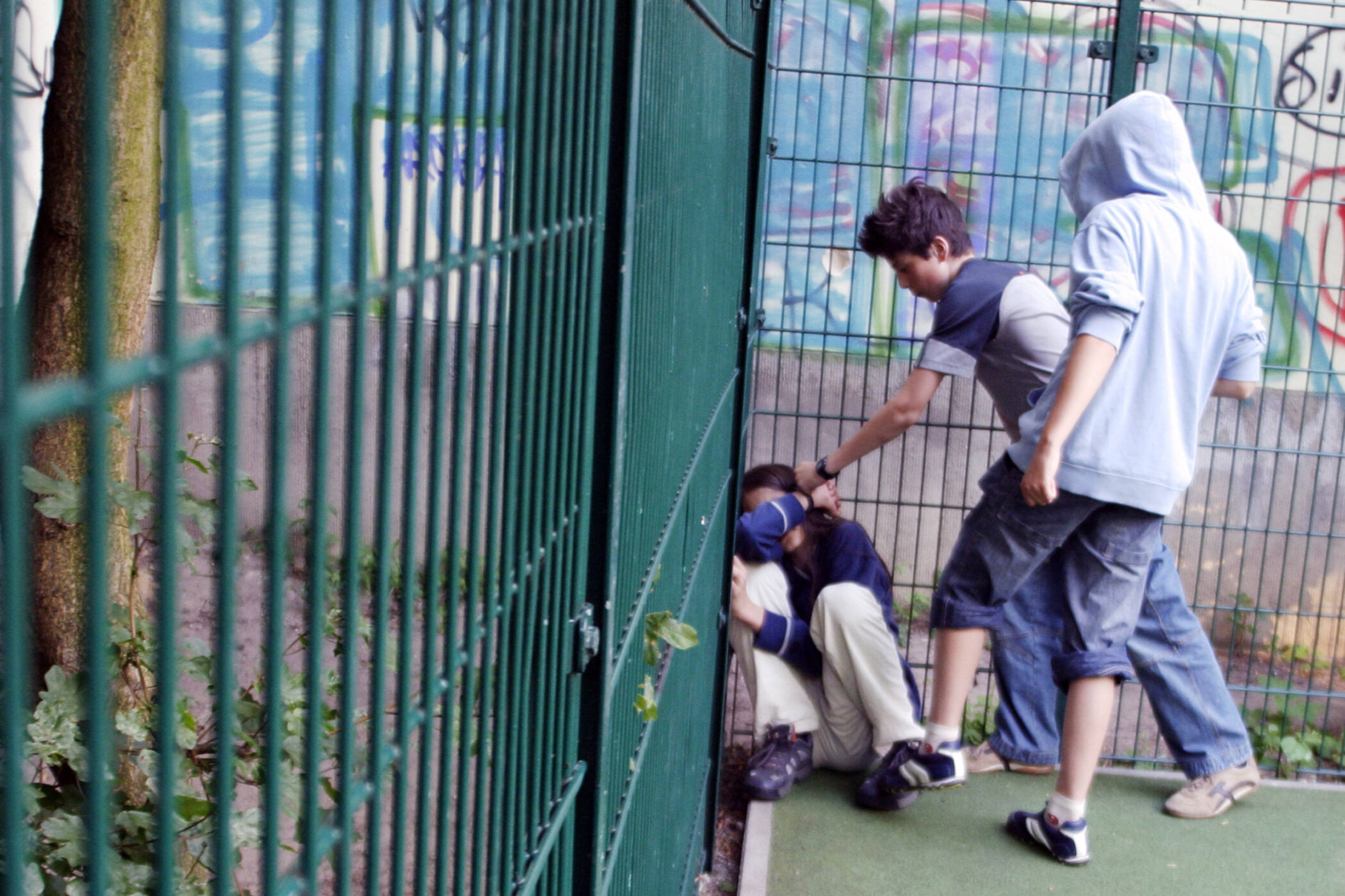 Drei Personen stehen nahe einem Gitterzaun, zwei stehen, eine Person hockt.
