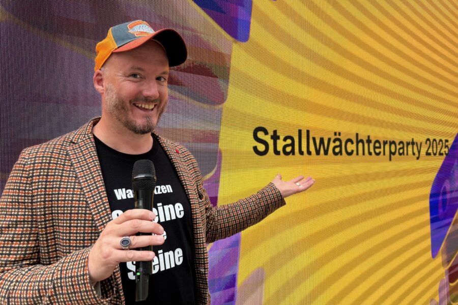 Mann mit Mikrofon vor gelbem Hintergrund mit Text: "Stallwächterparty 2025".