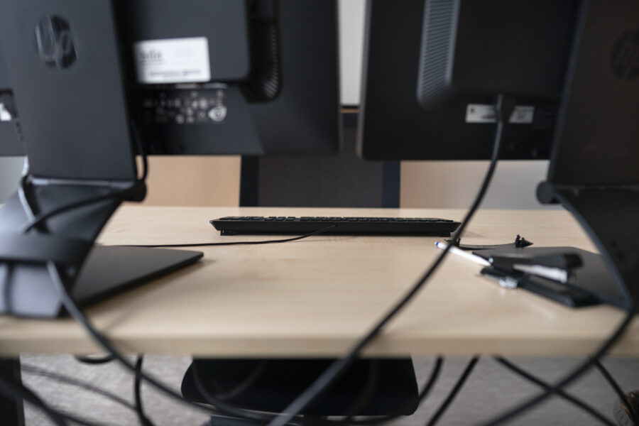 Bürotisch mit zwei Monitoren, Tastatur und Stift auf einem Notizblock.