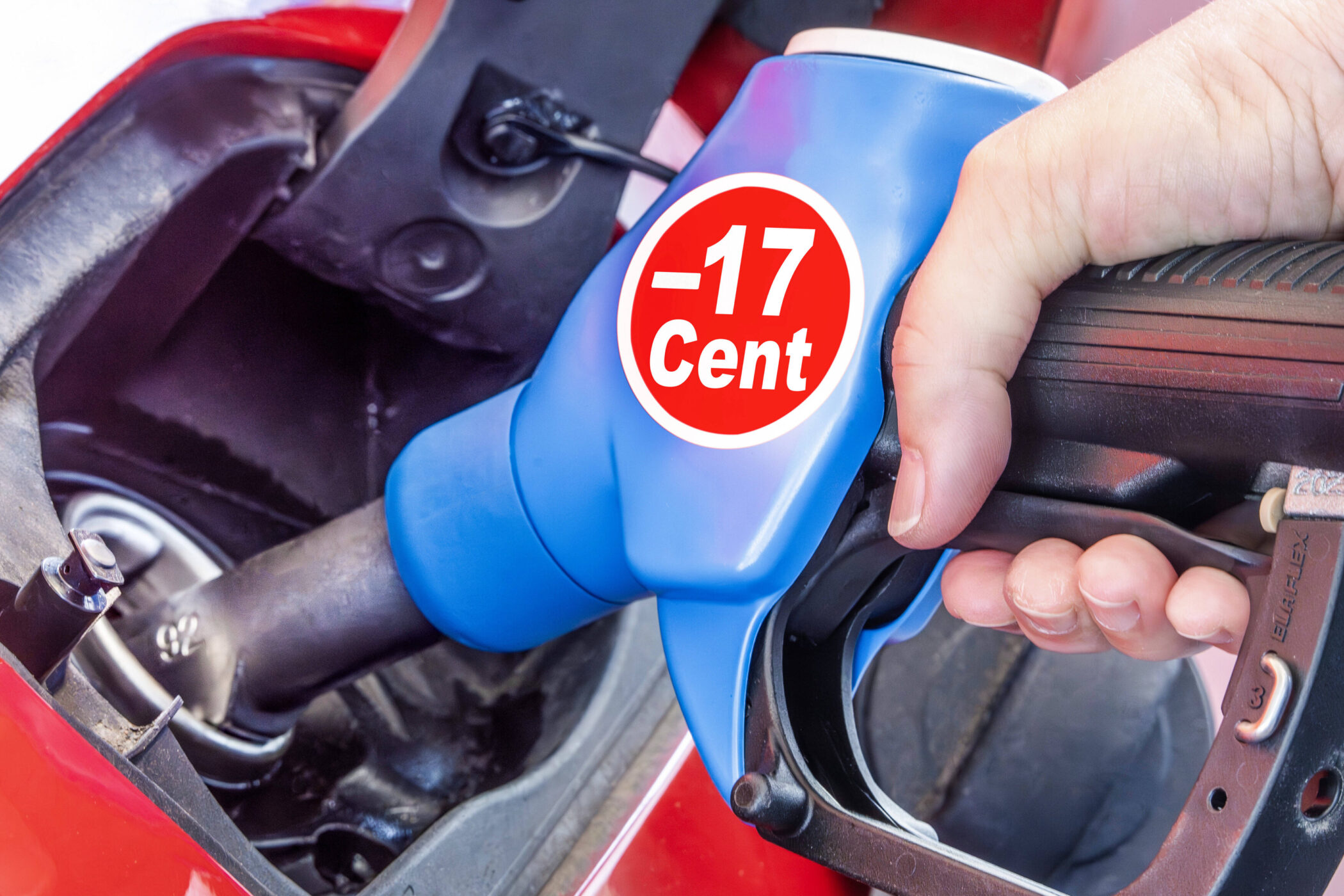 Blaue Zapfpistole im Tankstutzen, Aufschrift „-17 Cent“. Hand hält Griff.