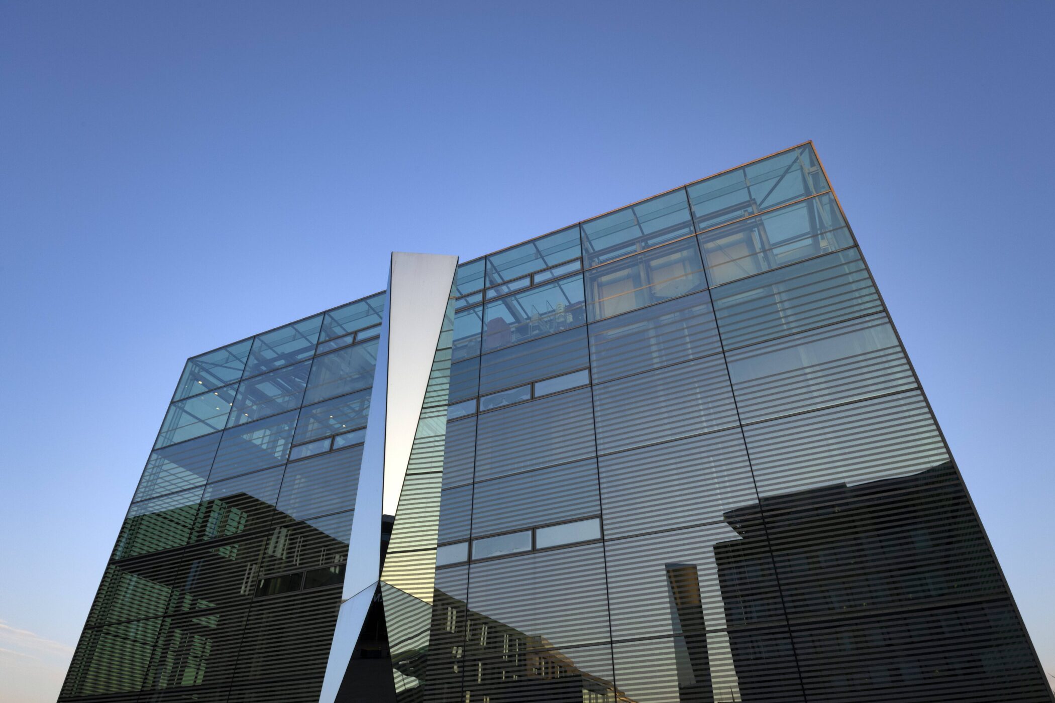 Moderne Glasfassade mit strukturierten Linien unter blauem Himmel.