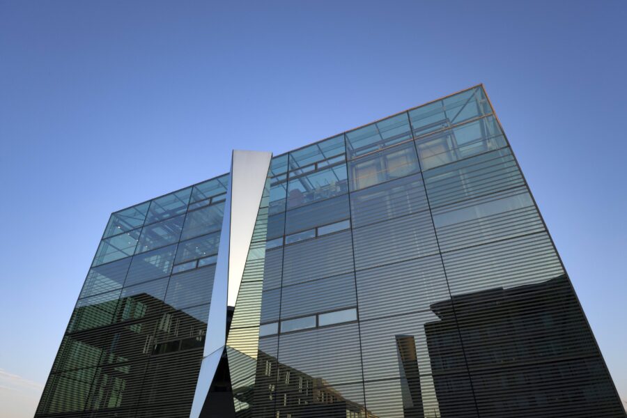 Moderne Glasfassade mit strukturierten Linien unter blauem Himmel.