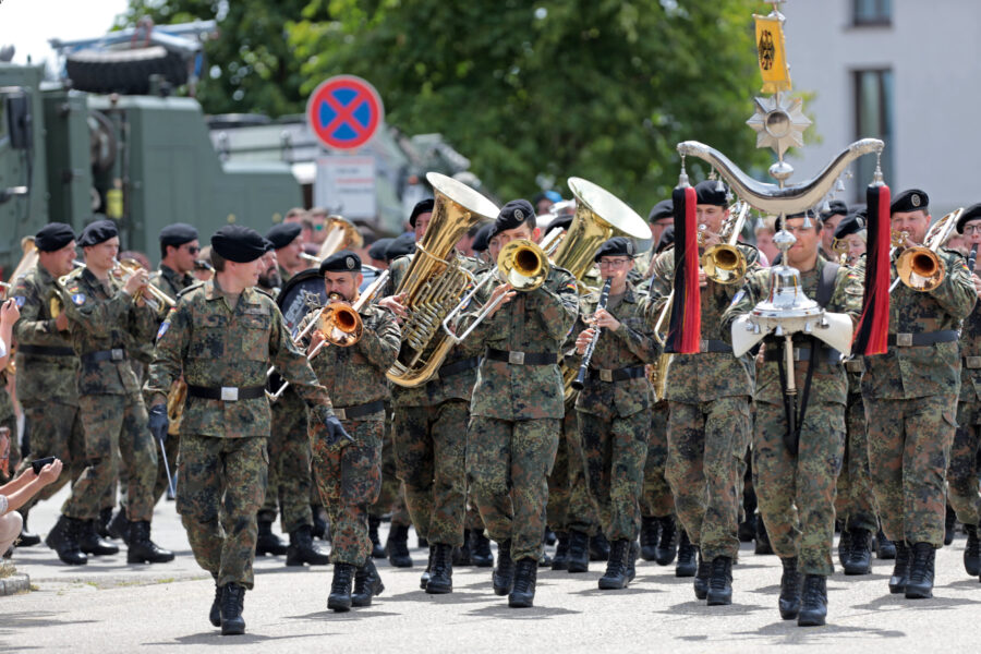 Gruppe von Soldaten in Uniformen marschiert und spielt Blasinstrumente.