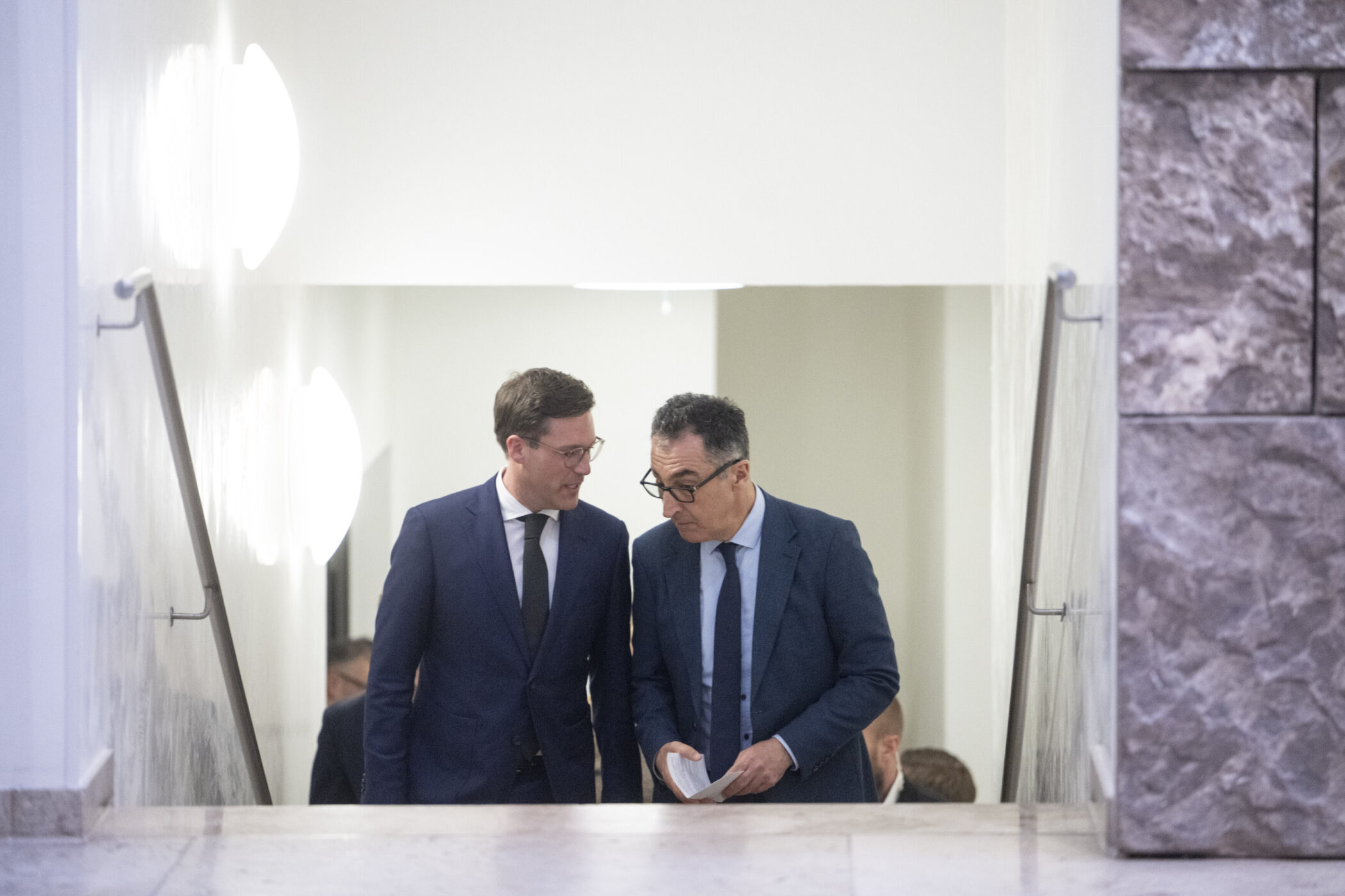 Zwei Männer in Anzügen sprechen auf einer Treppe miteinander.