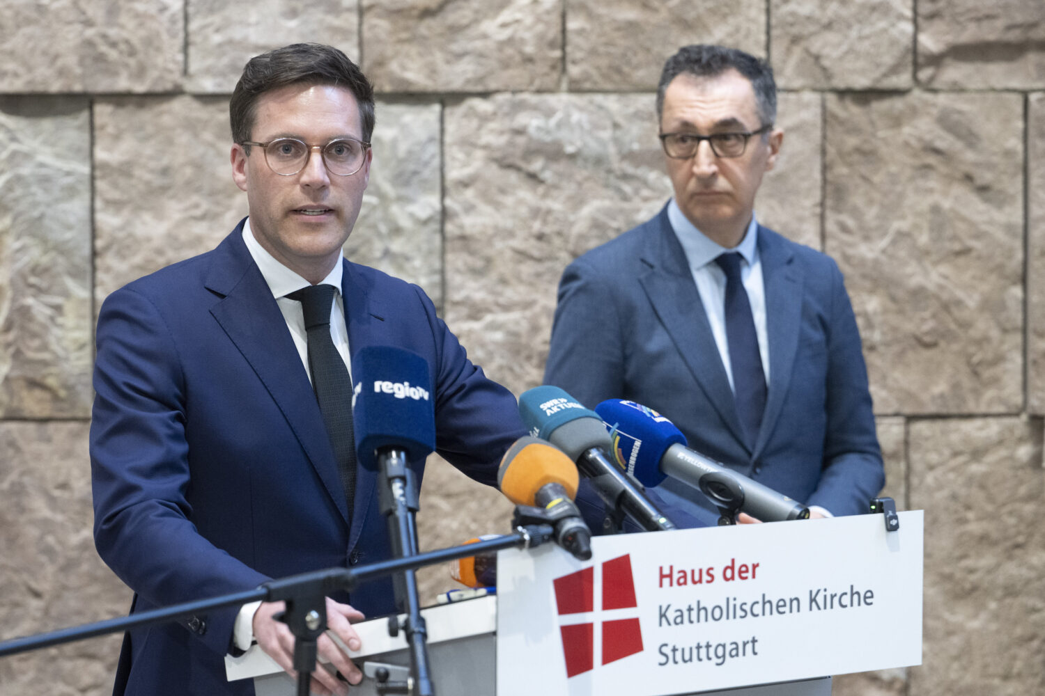 Zwei Männer im Anzug hinter einem Rednerpult mit Mikrofonen.