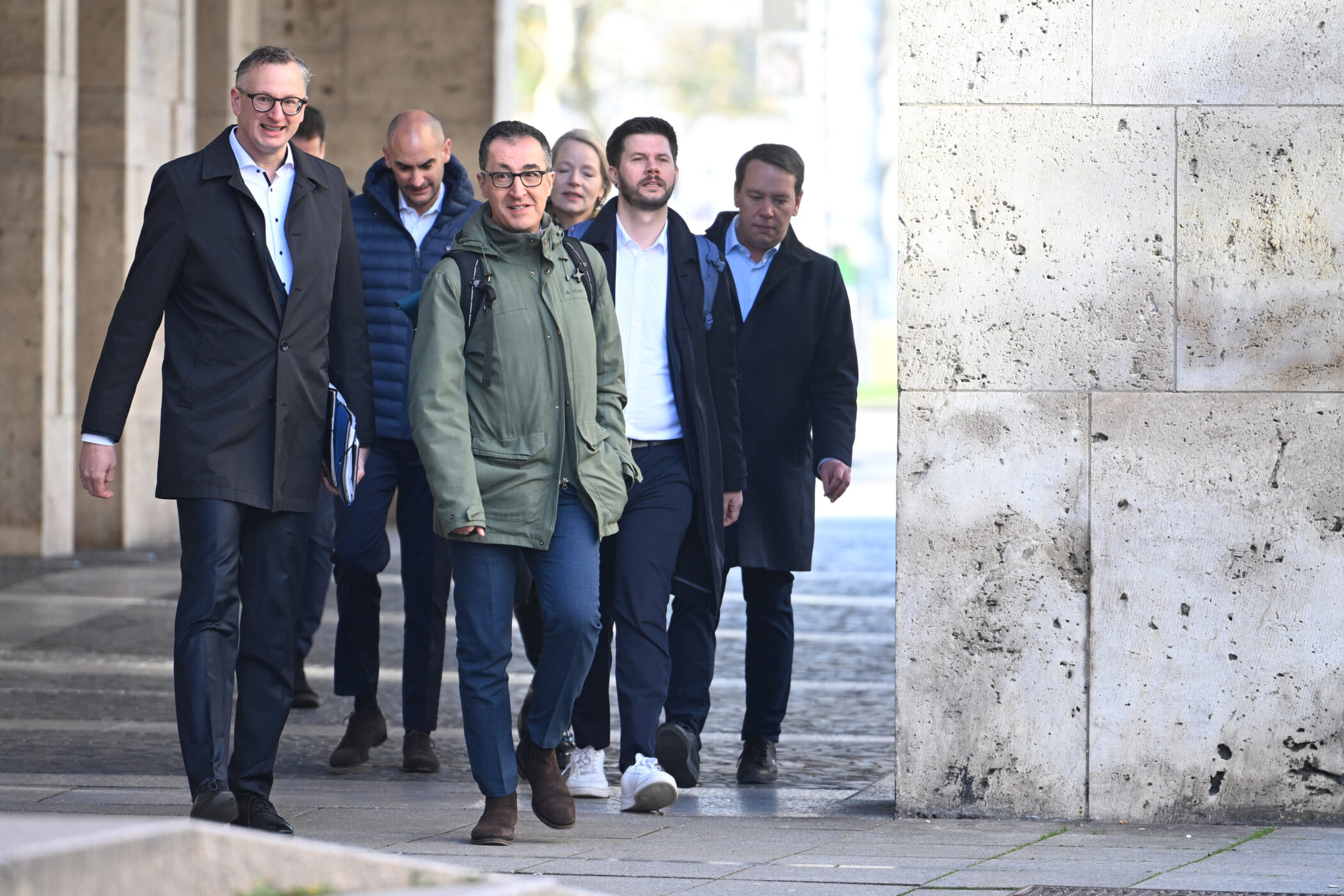 Sechs Männer gehen in einer Reihe auf einem Bürgersteig.