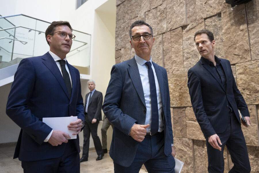 Vier Männer in Anzügen gehen nebeneinander in einem Gebäude.