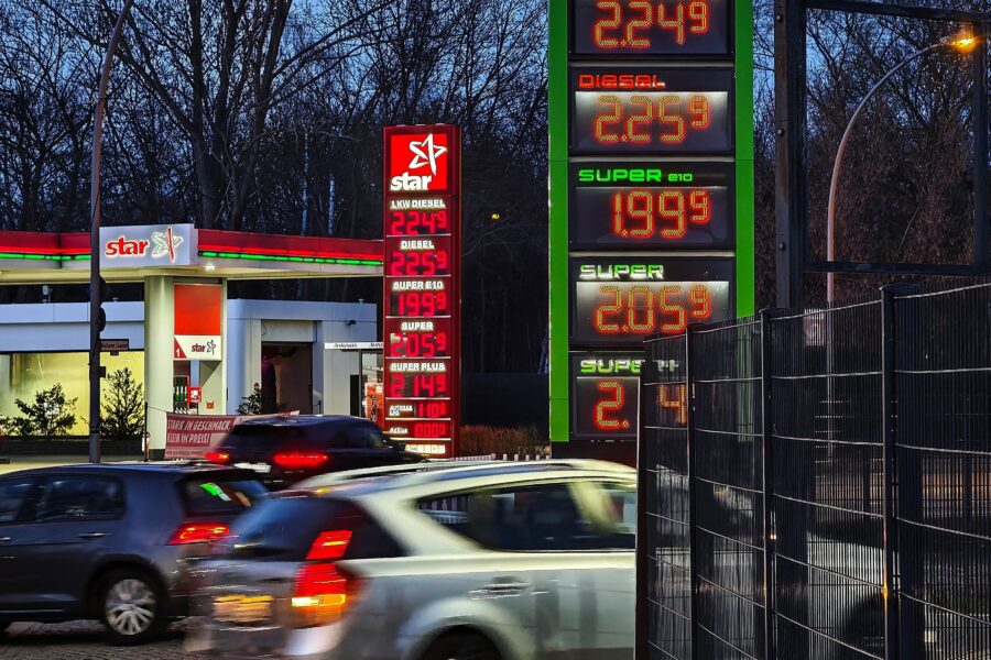 Tankstelle mit Preistafel im Hintergrund, mehrere fahrende Autos im Vordergrund.