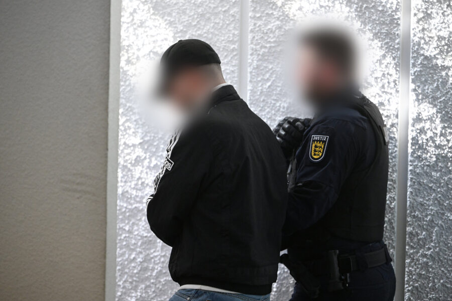 Zwei Personen stehen nebeneinander, eine trägt eine Jacke mit Aufschrift „Justiz“.