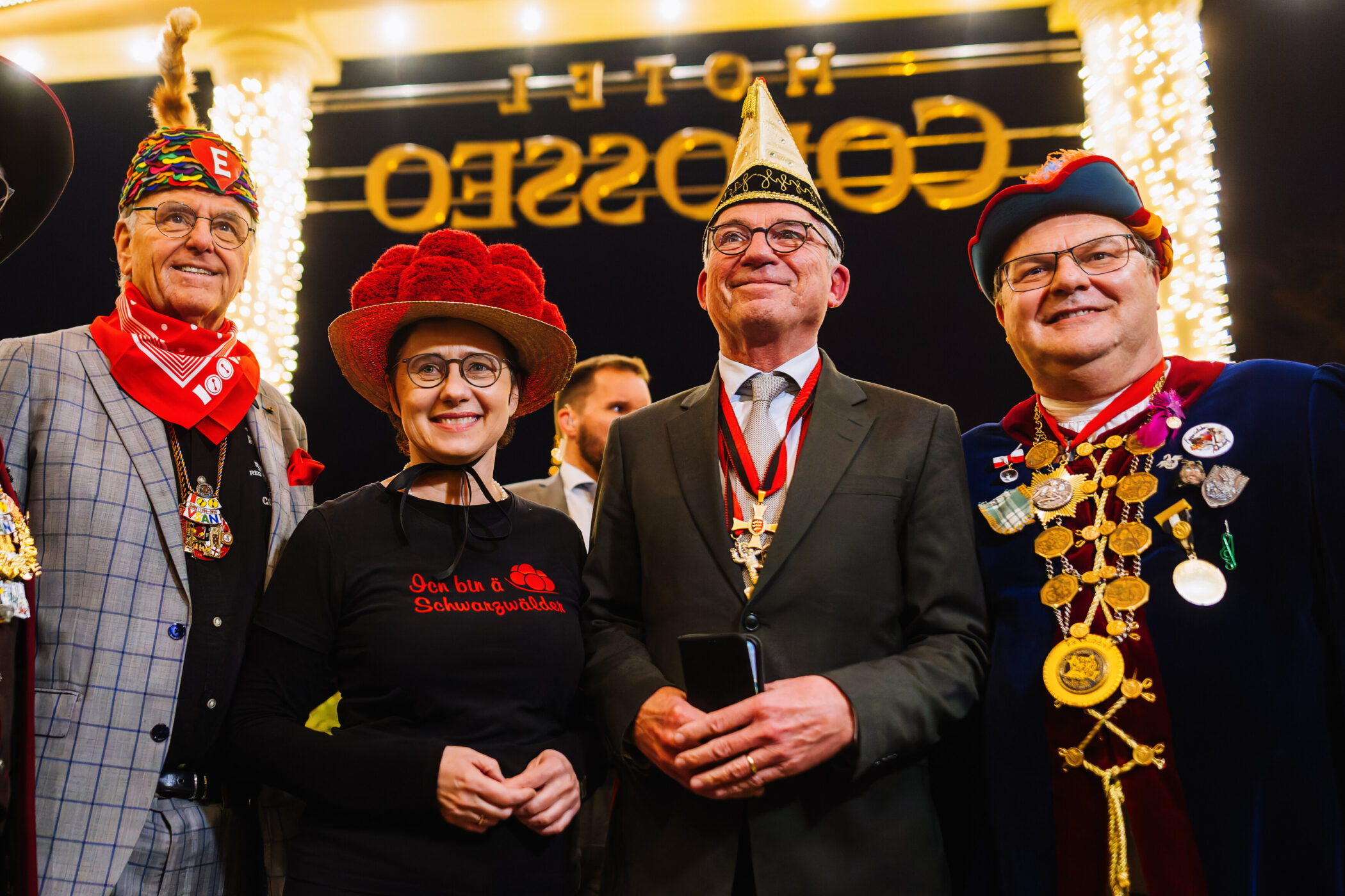 Vier Personen in festlicher Kleidung und Hüten stehen lächelnd zusammen.