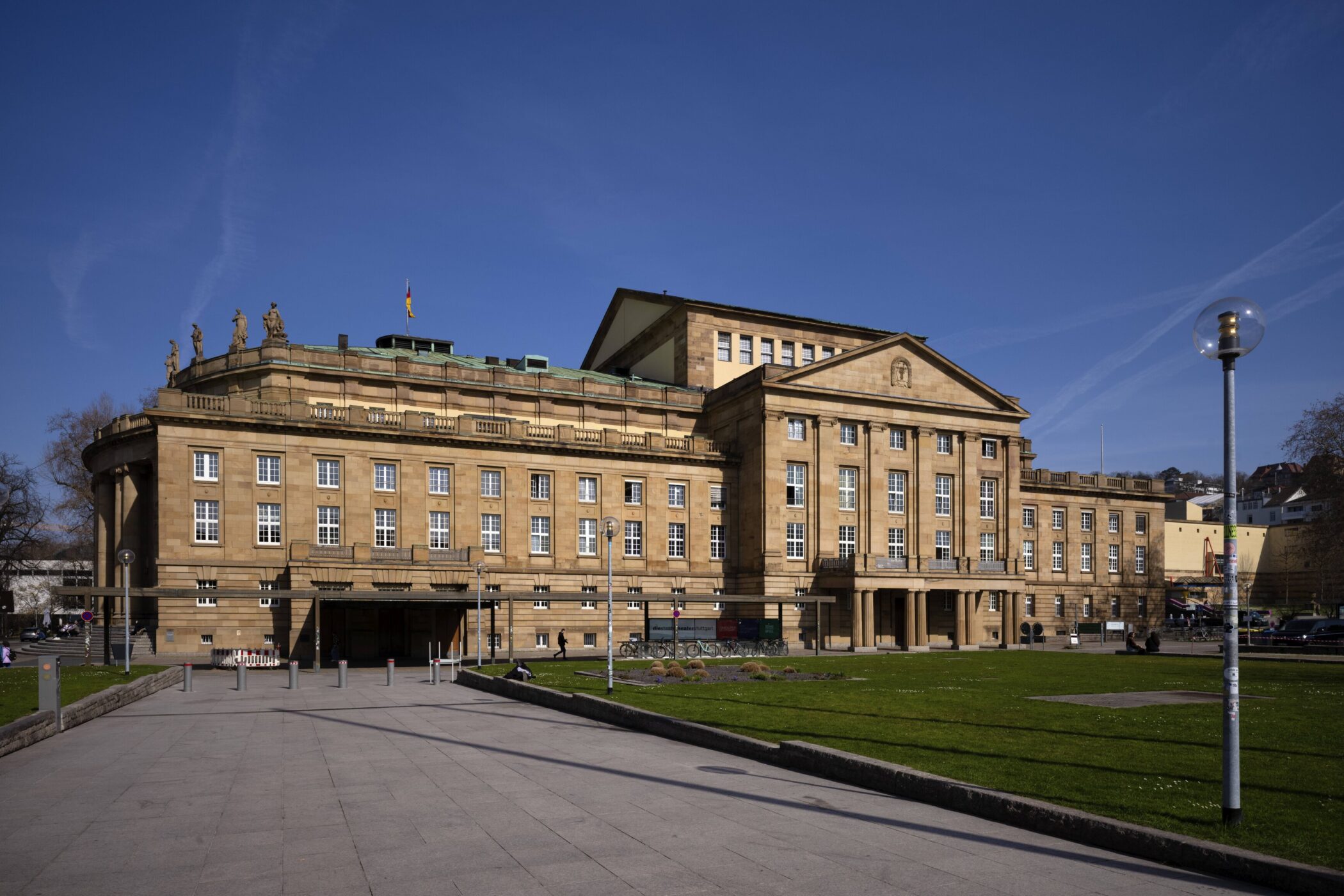 Historisches Gebäude mit Säulen, einer Fahne auf dem Dach und Figuren darauf.