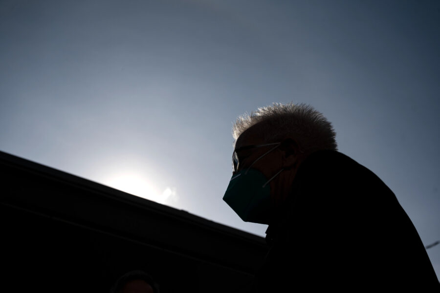 Person im Profil mit Maske vor heller Sonne im Hintergrund.