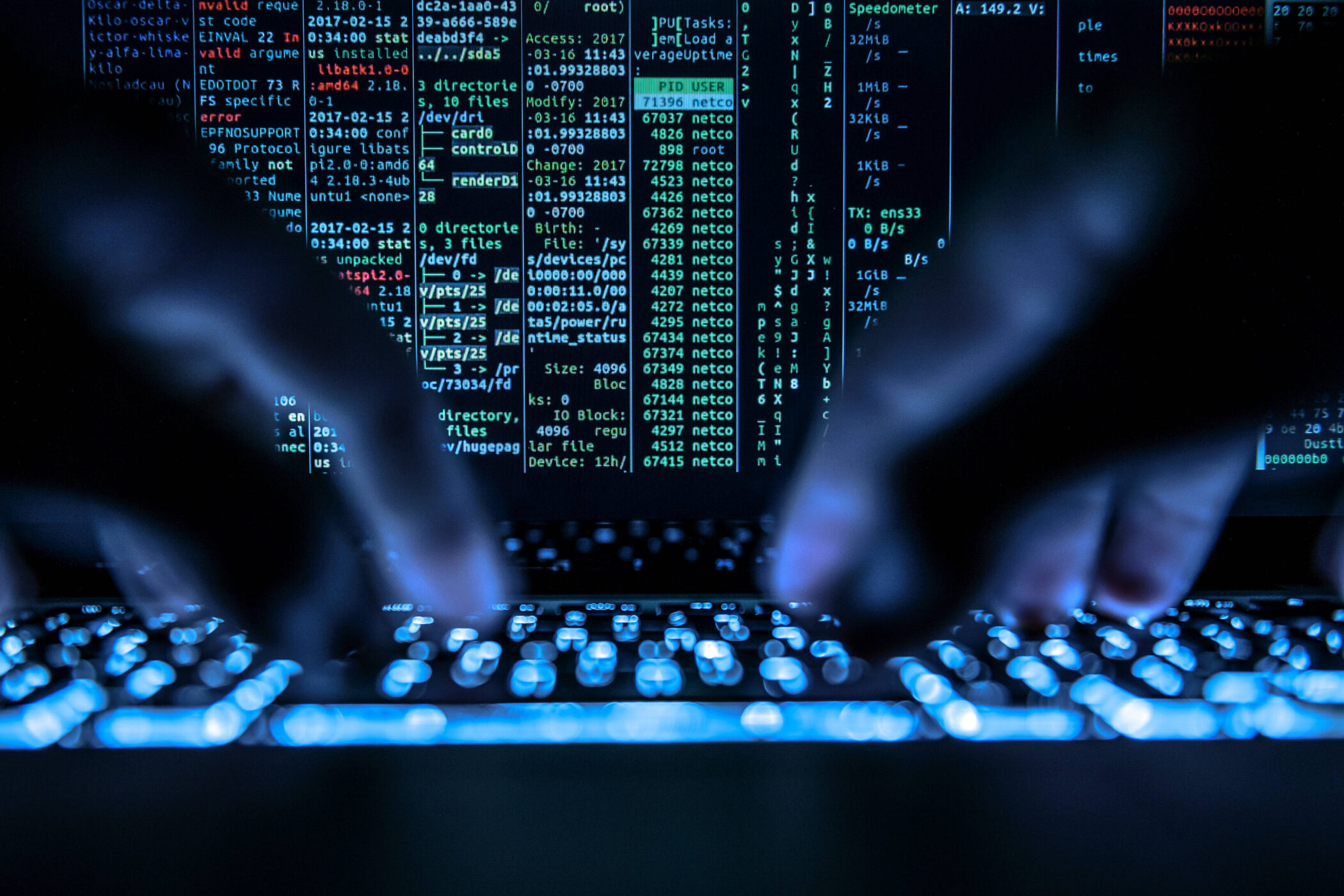 Hände tippen auf leuchtender Tastatur, Bildschirm mit Codezeilen im Hintergrund.