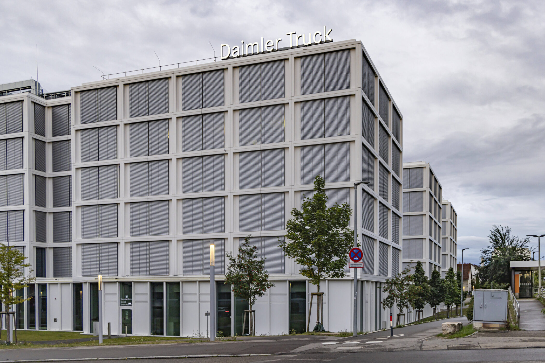 Gebäude mit Schriftzug "Daimler Truck", graue Fassade, Baumreihe, Straßenschild.