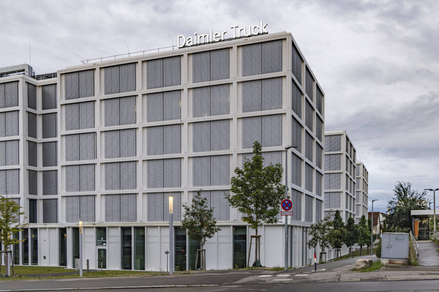 Gebäude mit Schriftzug "Daimler Truck", graue Fassade, Baumreihe, Straßenschild.