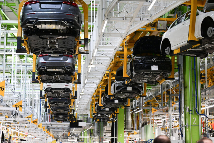 Autos auf gelben Hebebühnen in einer Fabrikhalle; grüne und weiße Strukturen.