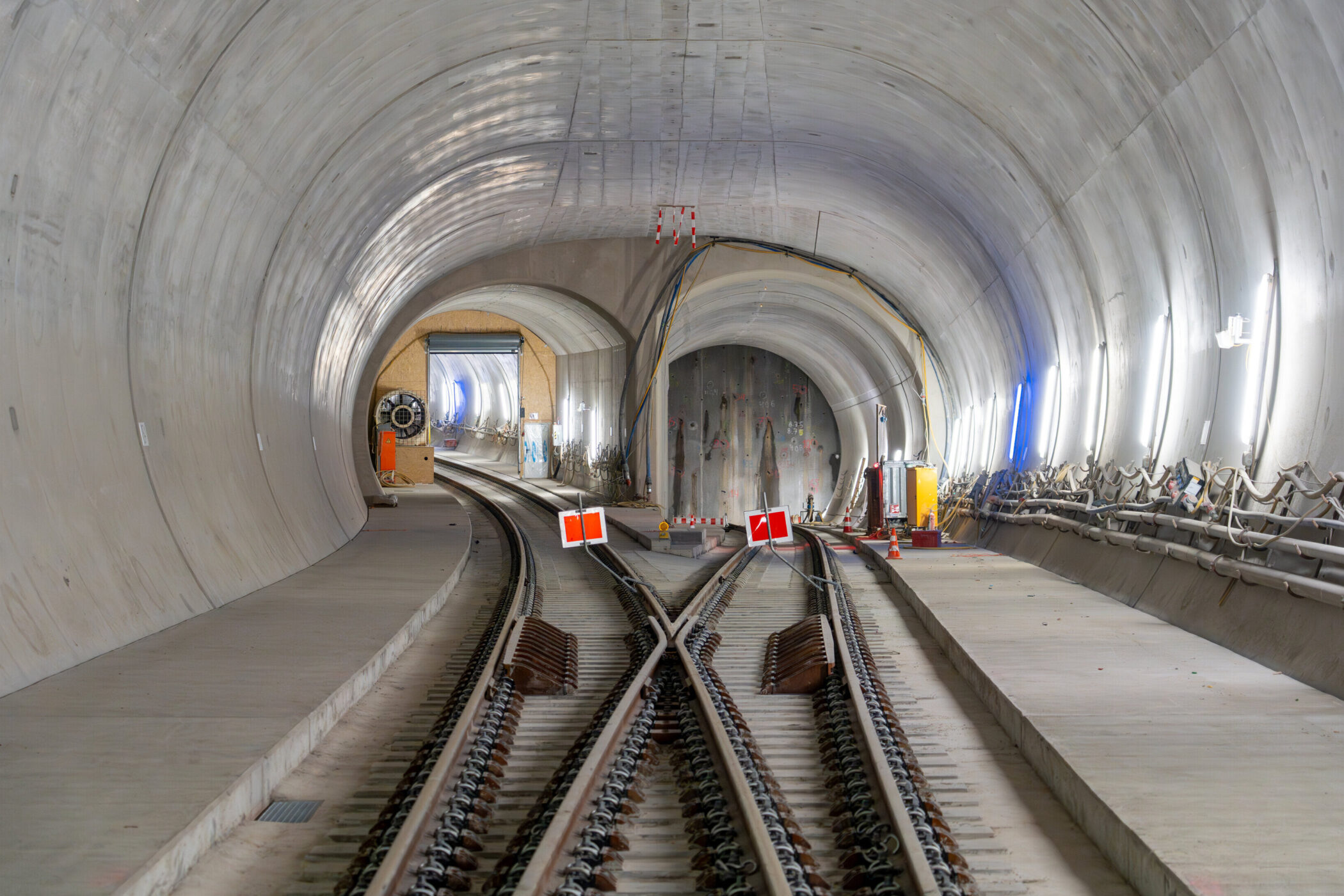 Zweigleisiger Eisenbahntunnel mit Baustellenabsperrungen und Beleuchtung.