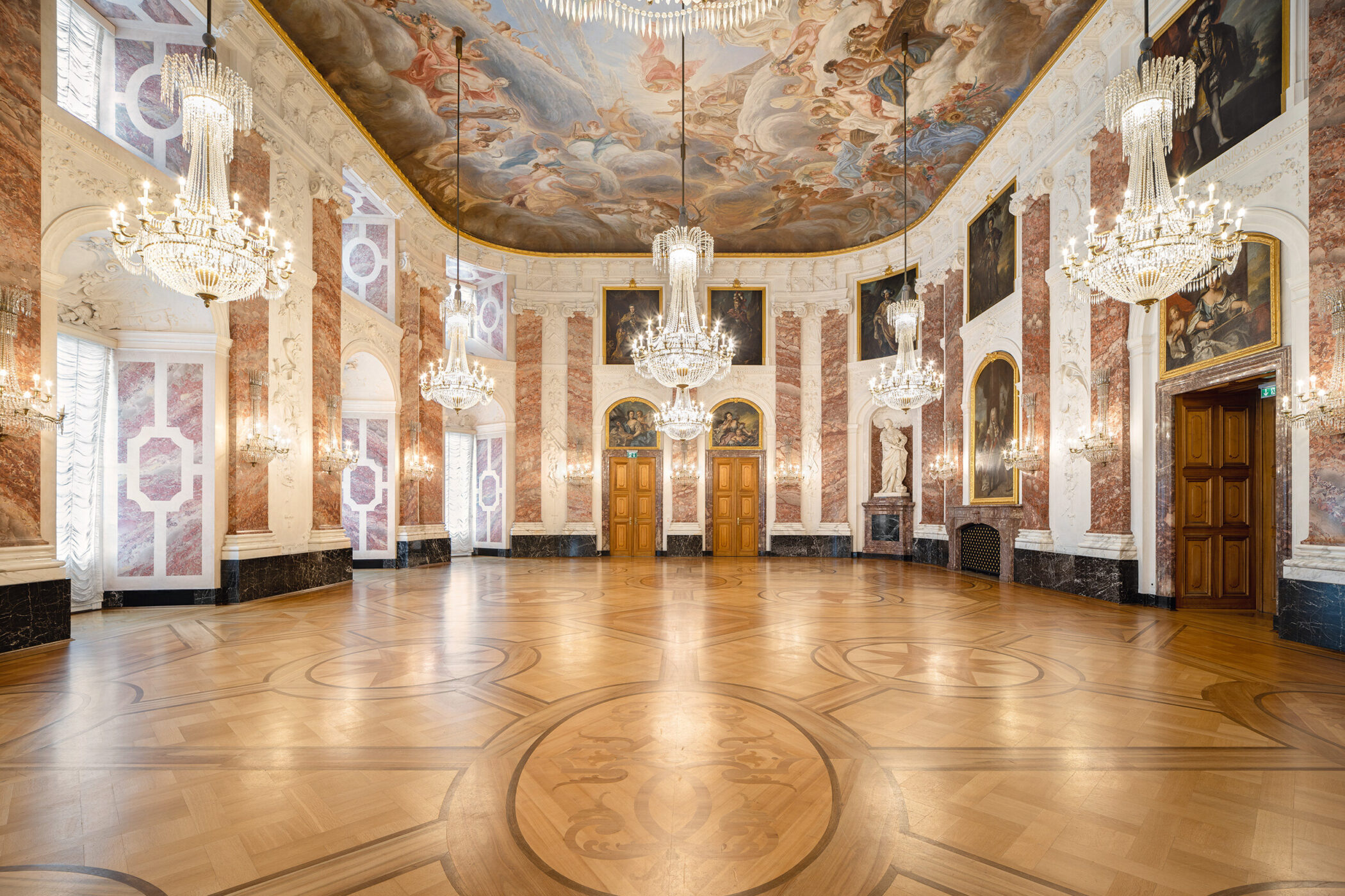 Prunksaal mit Gemälden, Kristallkronleuchtern, dekoriertem Holzboden und Deckenfresko.