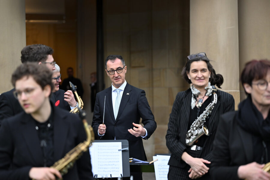 Mehrere Personen in Anzügen, einige halten Musikinstrumente.