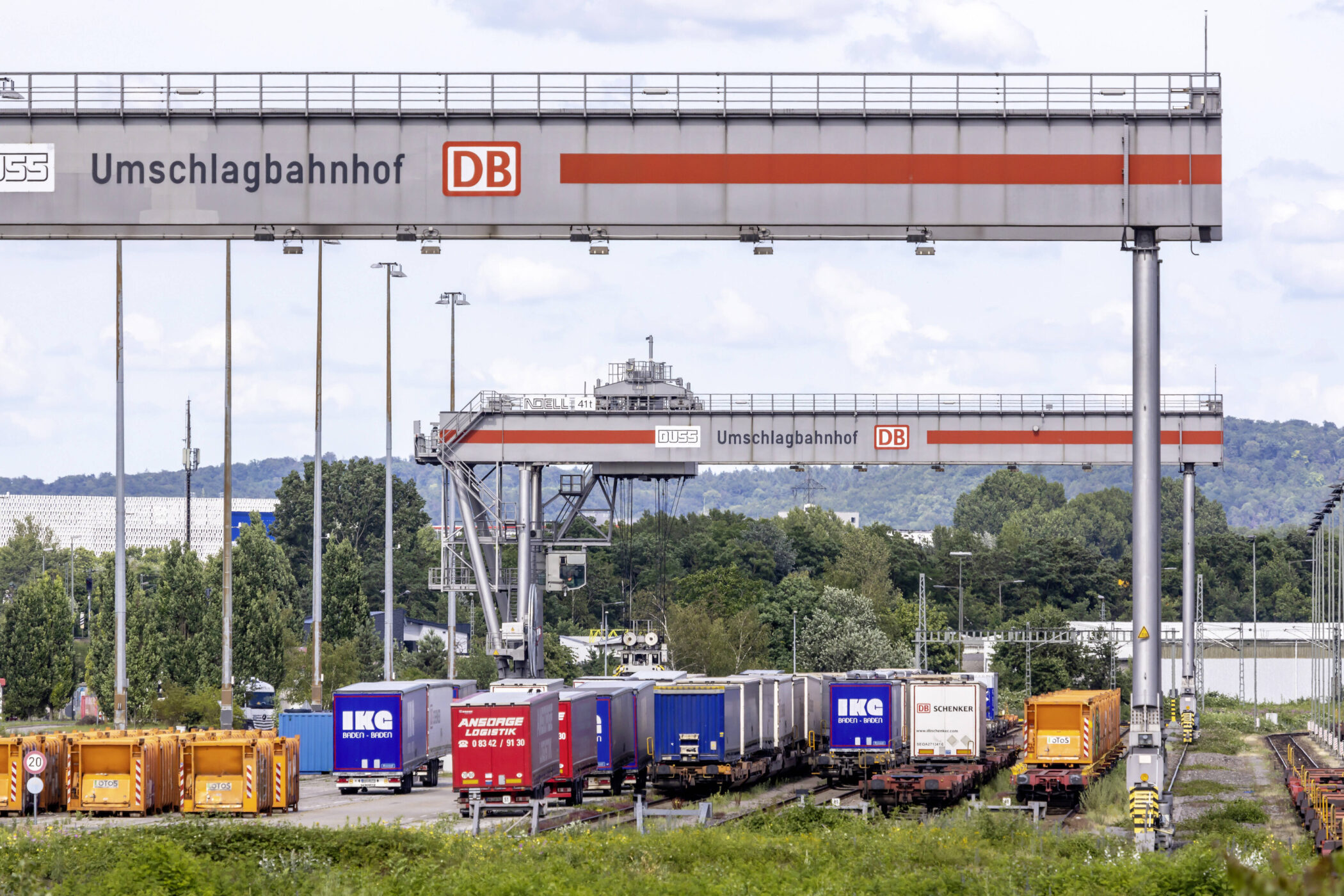 Umschlagbahnhof mit Containern, LKW-Aufliegern und zwei großen Kränen.