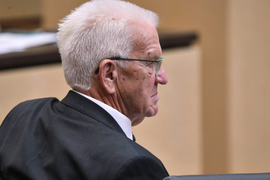 Älterer Mann im Anzug sitzt, Seitenansicht, weißes Haar, Brille.