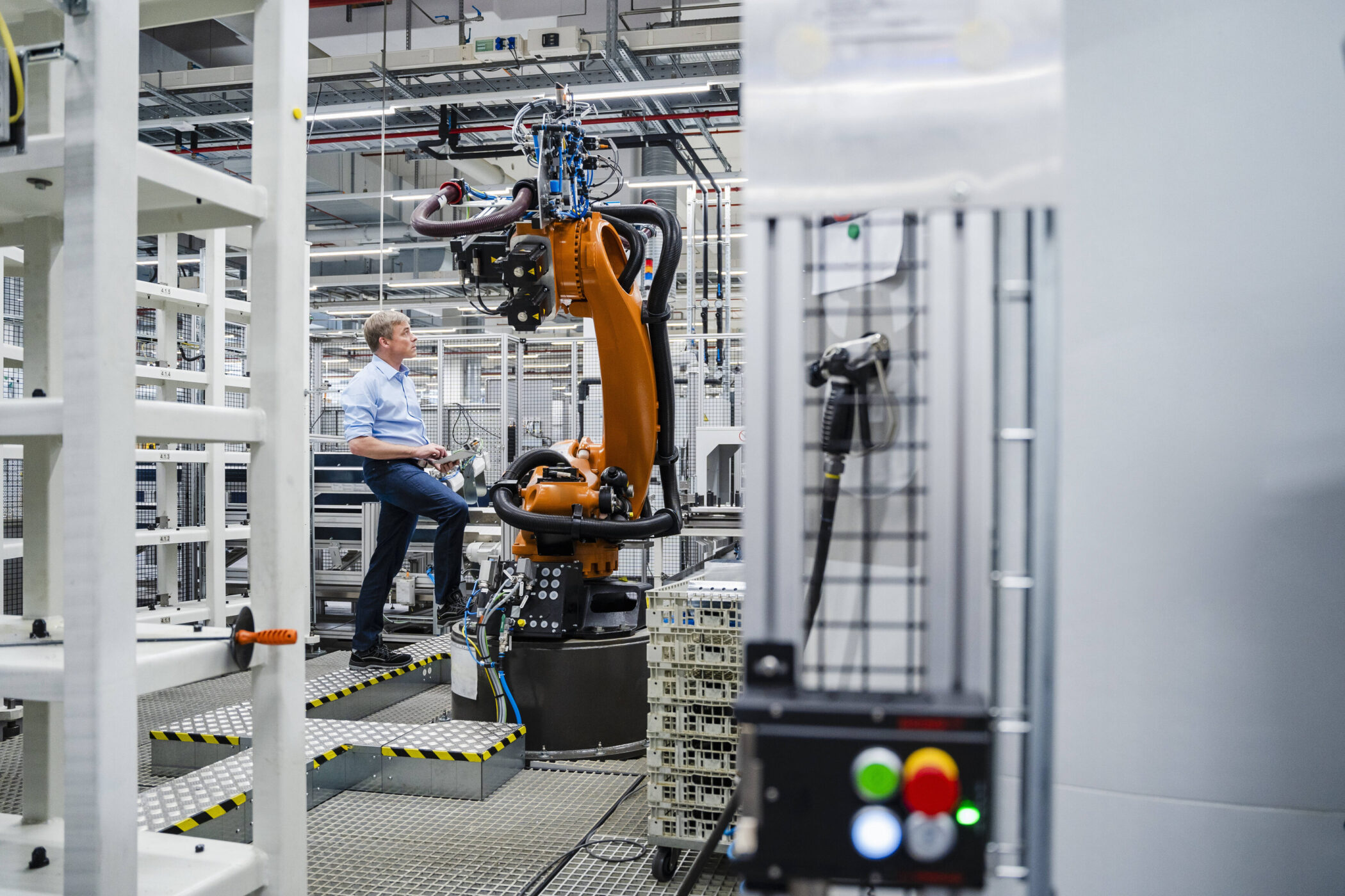 Person bedient orangefarbenen Industrieroboter in Fabrikumgebung.