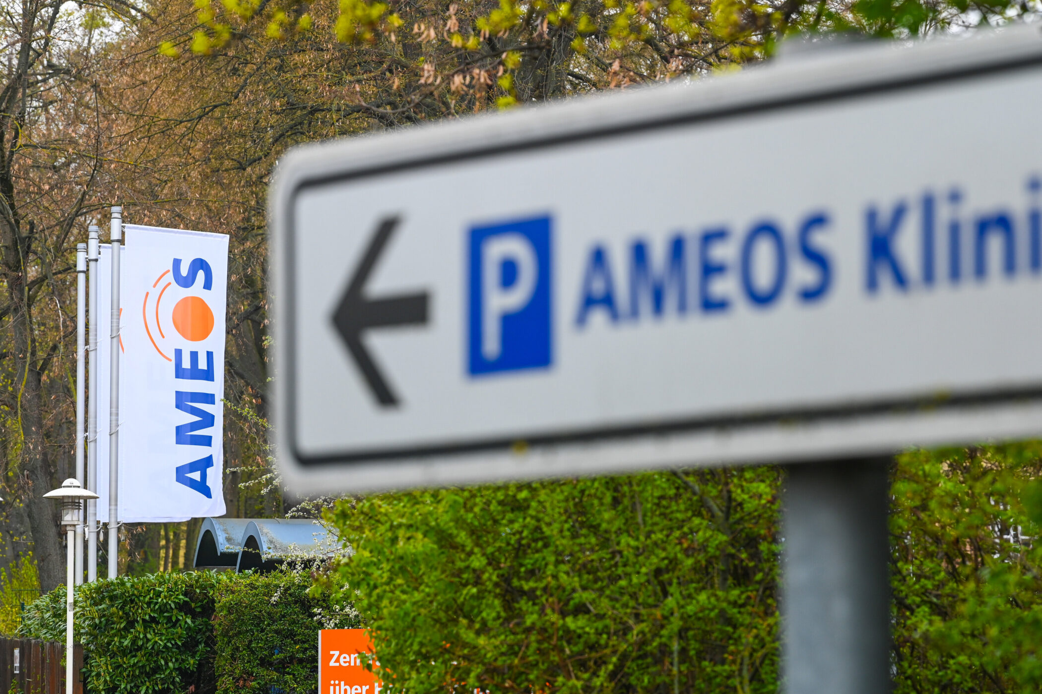 Wegweiser zu „AMEOS Klinik“ mit Pfeil, Hintergrund Bäume, weiße Fahne.