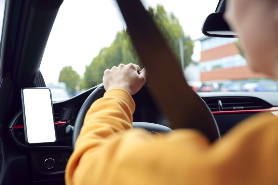 Person fährt Auto, hält das Lenkrad mit beiden Händen, weißer Bildschirm links.