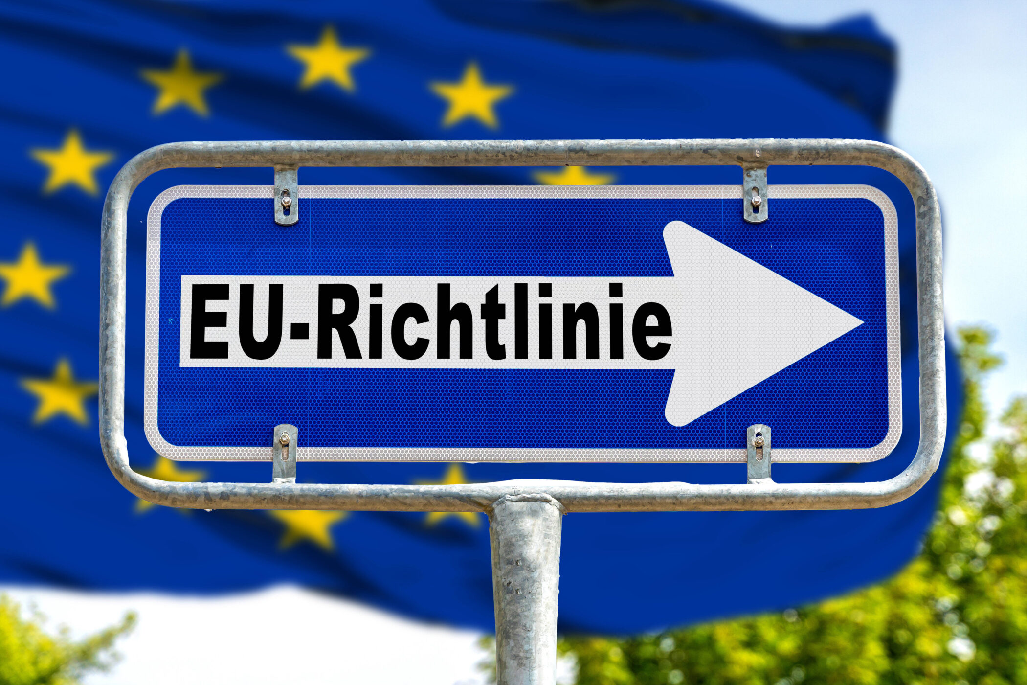 Blaues Schild mit Aufschrift "EU-Richtlinie" und Pfeil, EU-Flagge im Hintergrund.