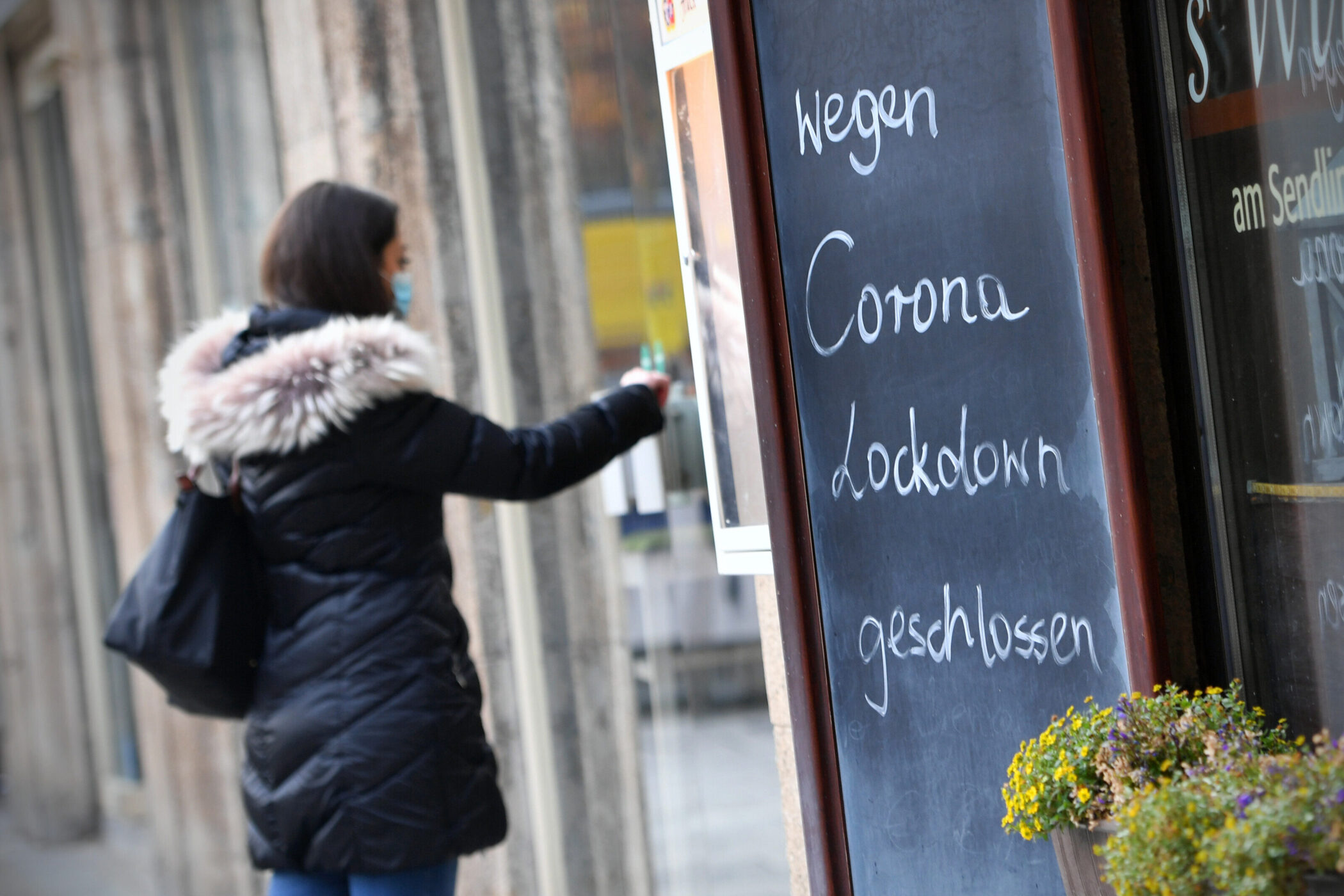 Eine Person mit Maske vor Schild: „Wegen Corona Lockdown geschlossen“.