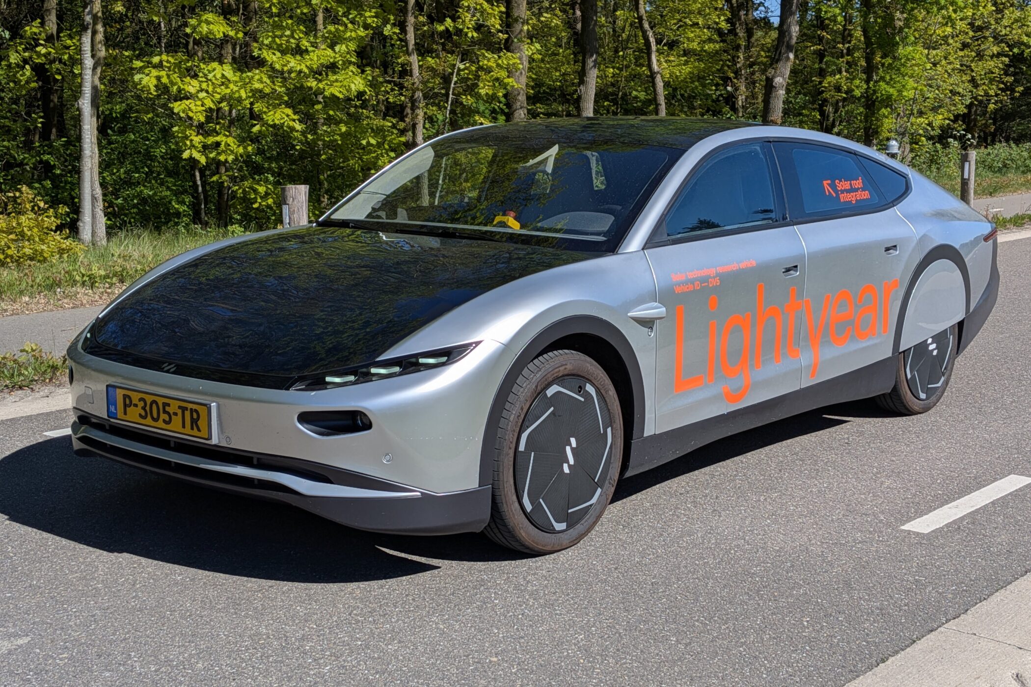 Silberfarbiges Auto mit Schriftzug "Lightyear" auf der Seite, Wald im Hintergrund.