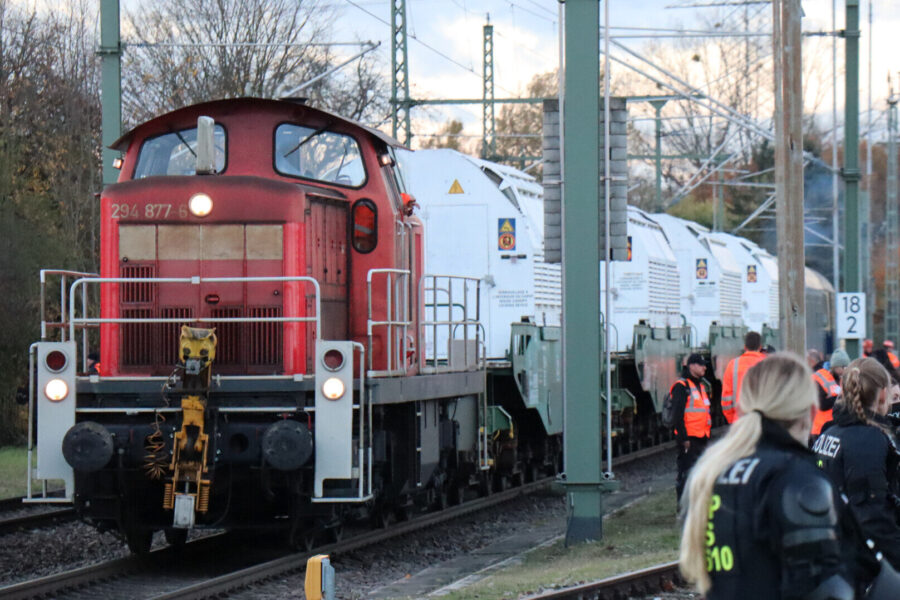 Rote Lokomotive zieht weiße Waggons, umgeben von Personen in Warnwesten und Uniformen.
