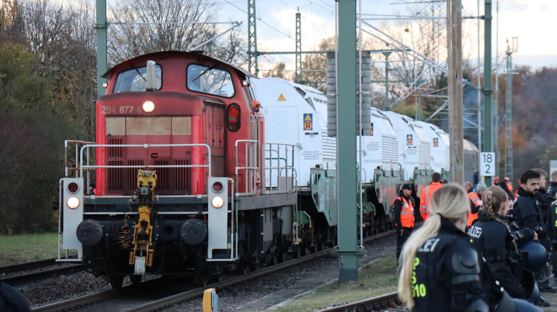 Rote Lokomotive zieht weiße Waggons, umgeben von Personen in Warnwesten und Uniformen.