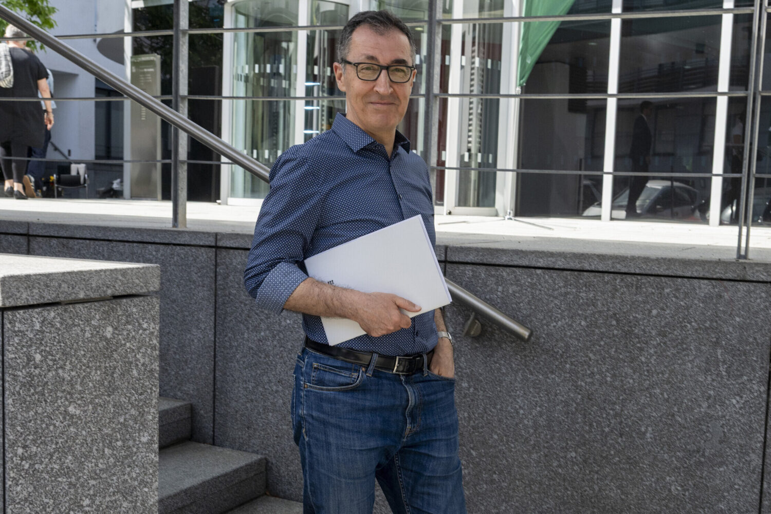 Mann mit Brille und Aktenmappe steht draußen vor einem Gebäude.