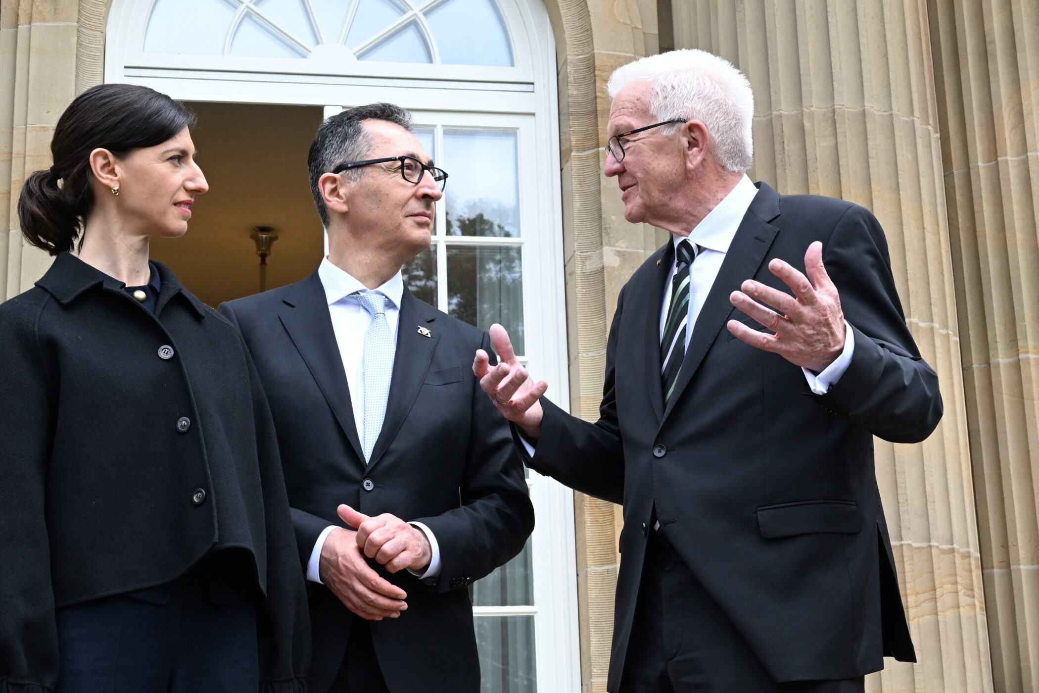 Drei Personen in Anzügen stehen vor einer Tür und unterhalten sich.