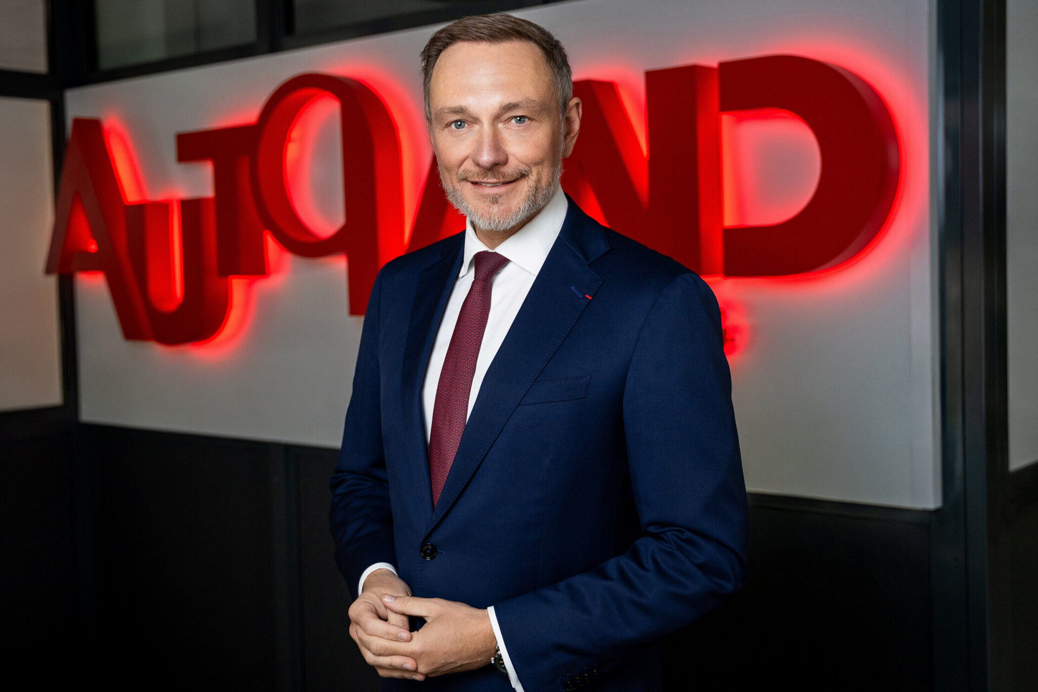 Mann in Anzug vor leuchtendem roten Schriftzug „AUTOAND“.