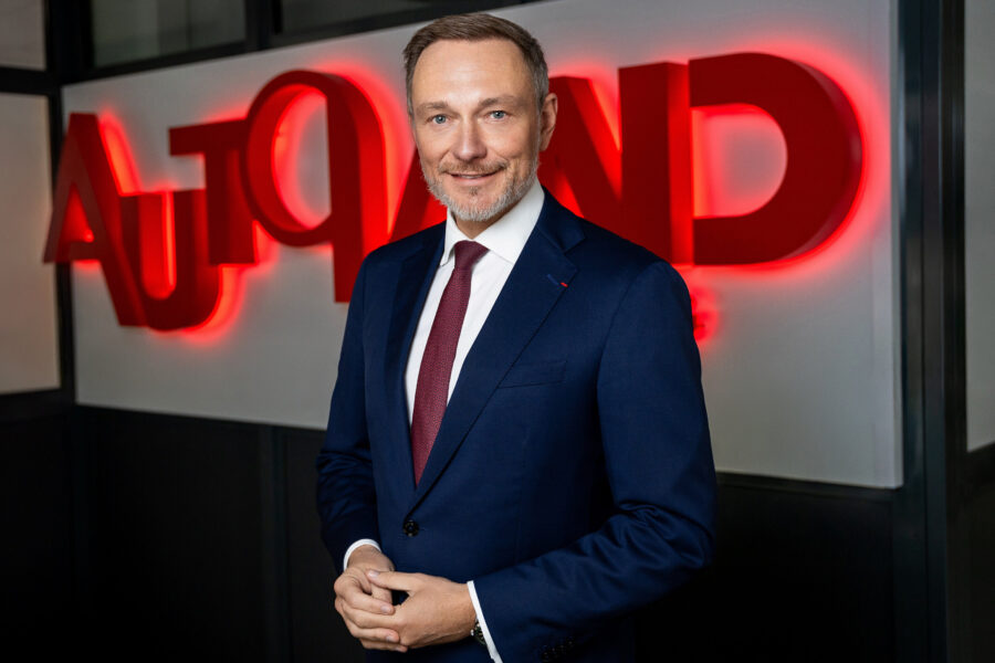 Mann in Anzug vor leuchtendem roten Schriftzug „AUTOAND“.